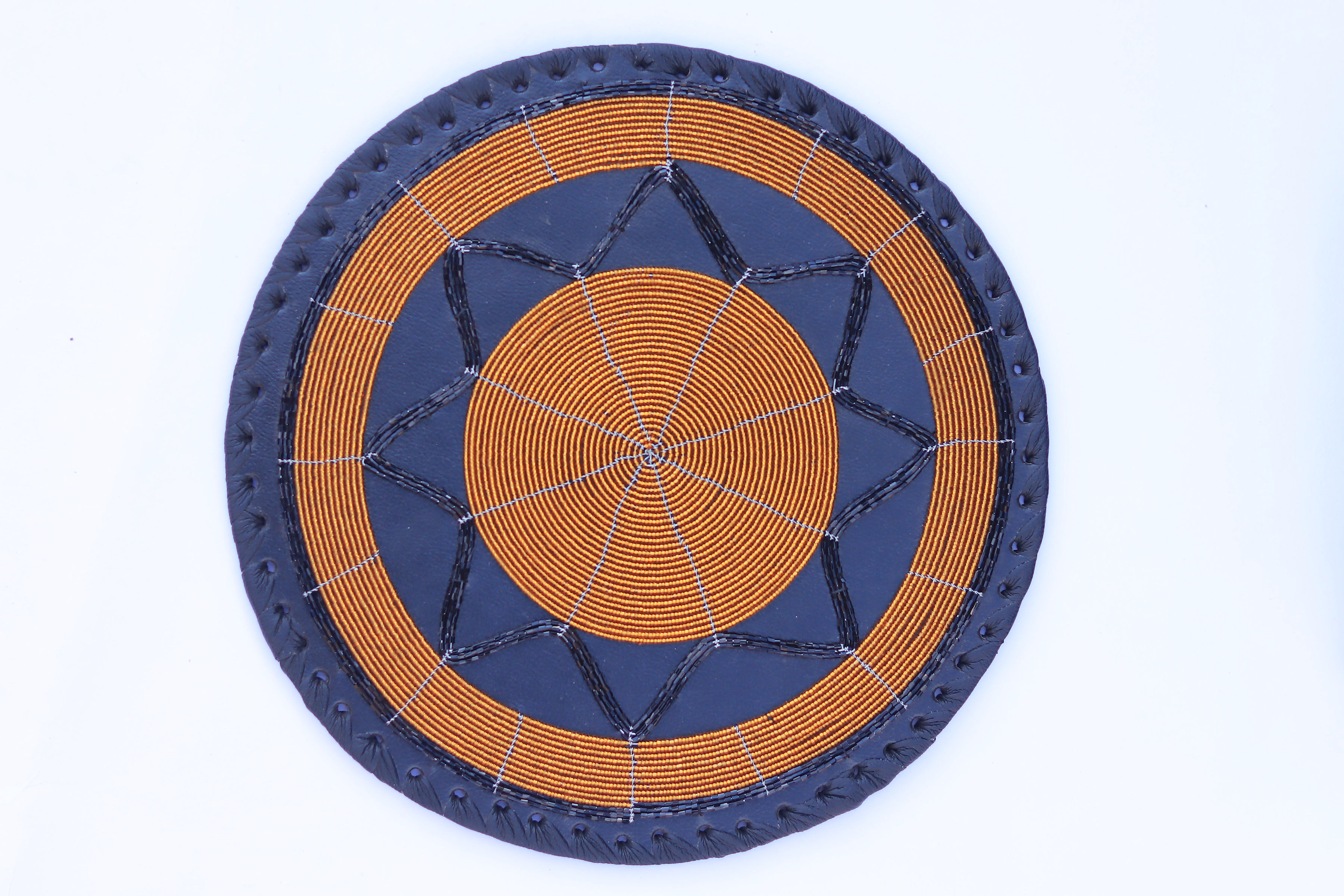 Round beaded place mat with amber and gold star pattern on navy leather with black braided edge