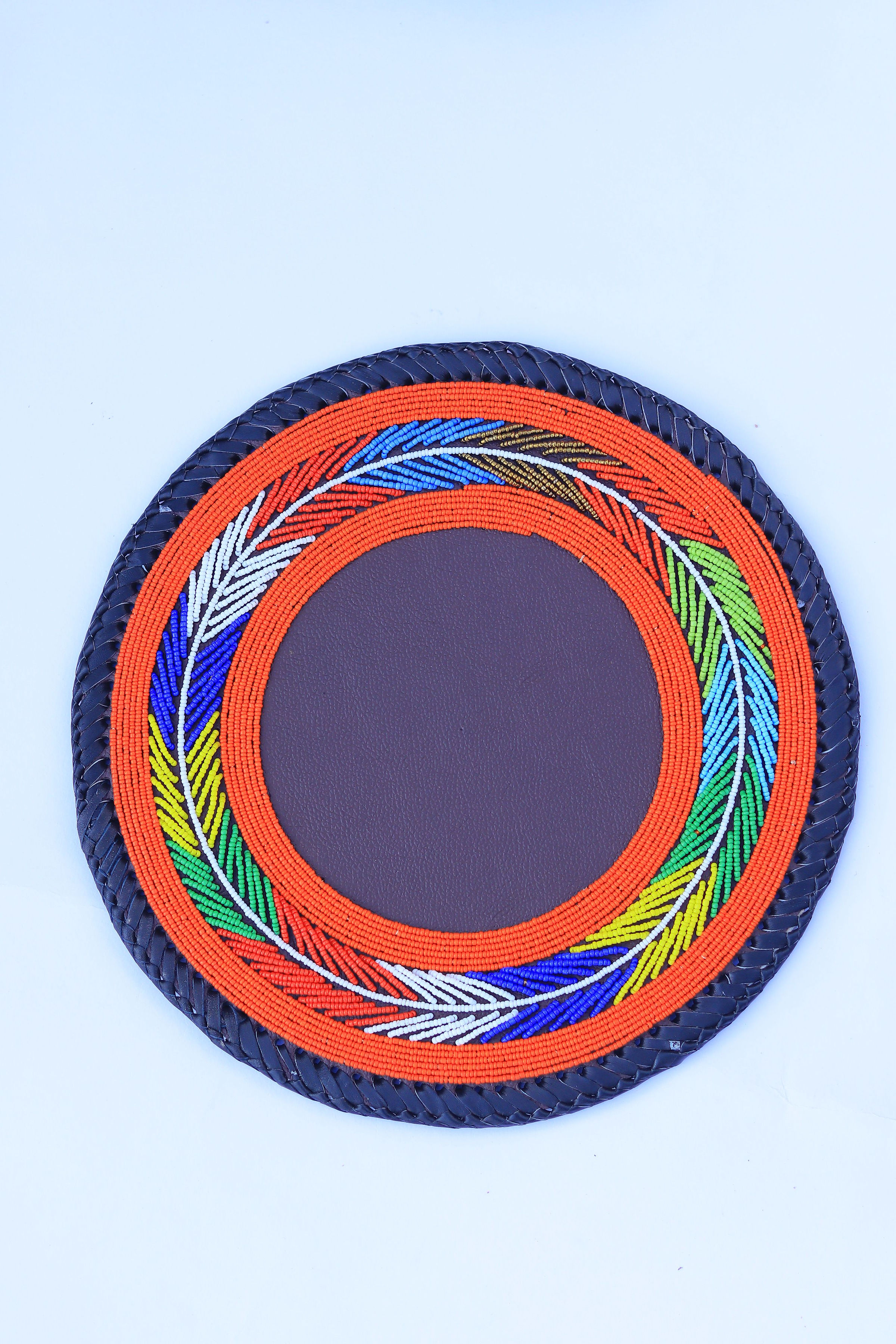Round beaded place mat with orange base and rainbow leaf wreath on black braided edge