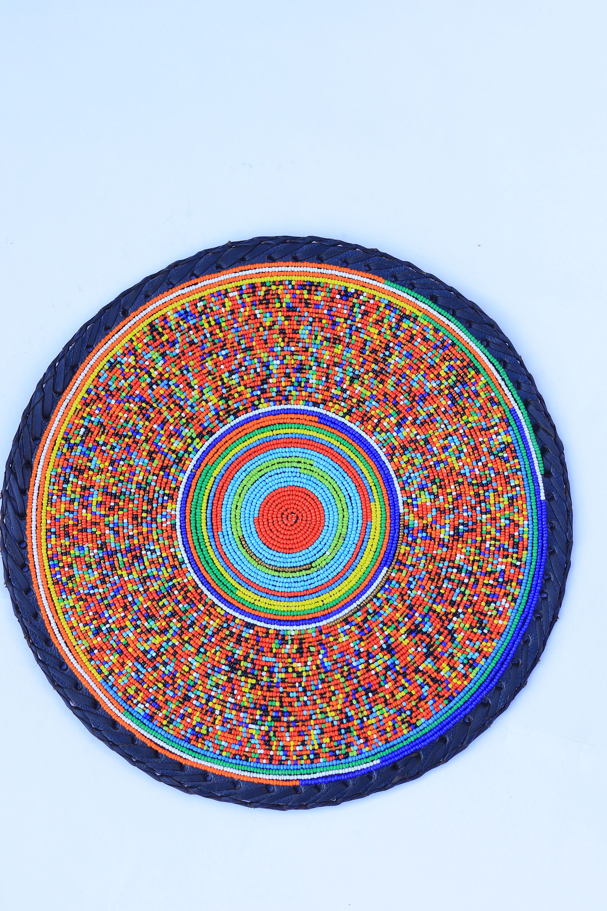 Fully beaded round place mat with rainbow sunburst pattern and navy braided edge